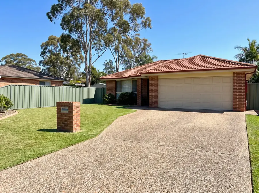 An exposed aggregate concrete driveway, small stones showing across its whole surface, running from a double garage past a lawn and brick letterbox to the street